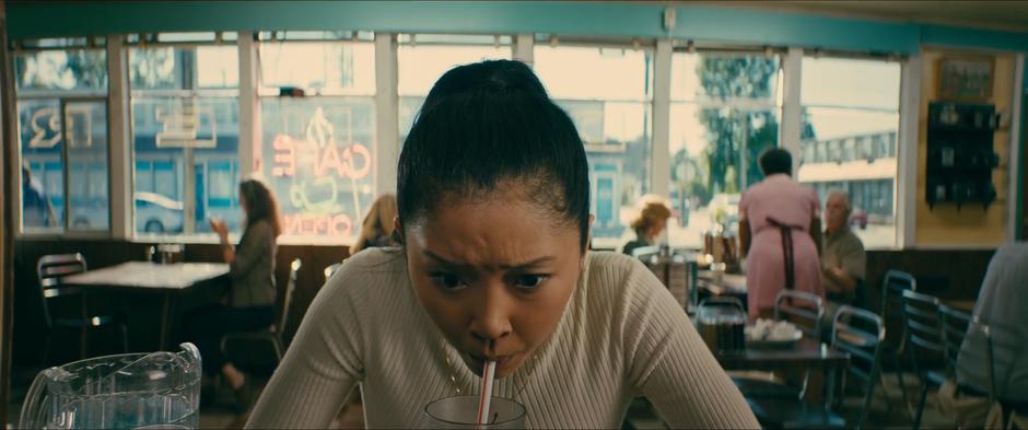 Lara Jean takes a big gulp of her soda while sitting at the counter.