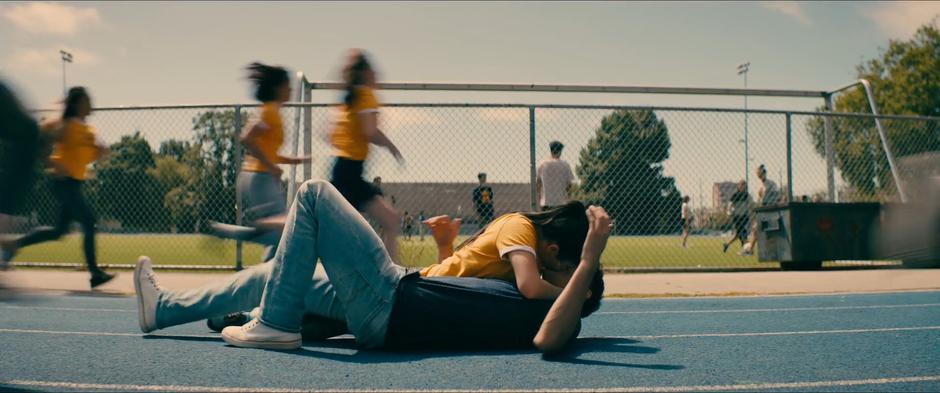 Lara Jean kisses Peter on the ground while the other members of track run past them.