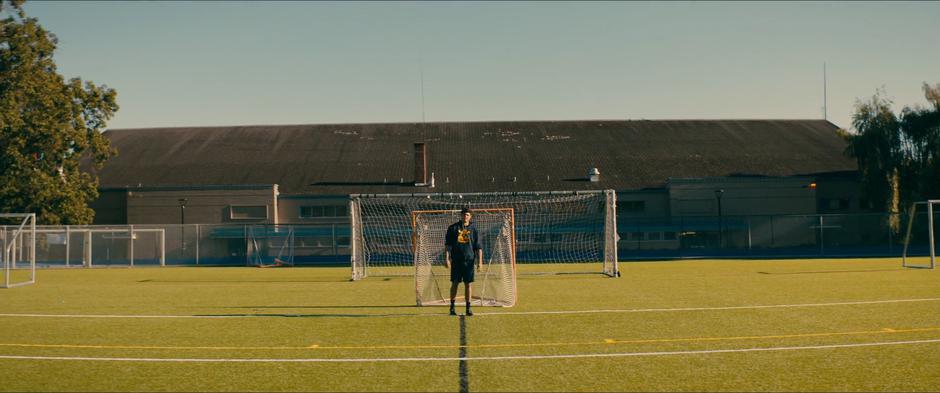 Peter watches Lara Jean from across the field as he stands in front of the goal after lacross practice.