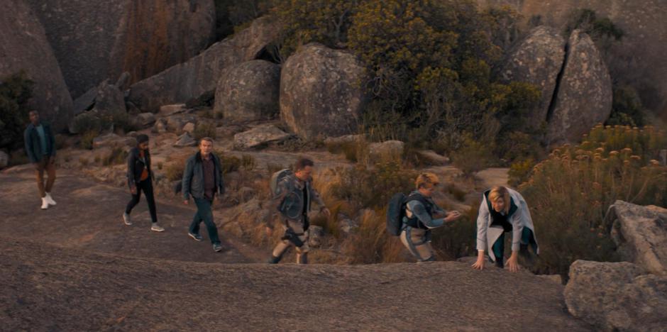 The Doctor climbs up onto the rocks at the front of the whole group.