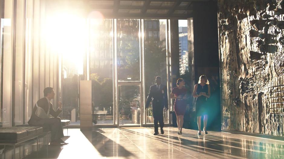 Ben Thompson stands up as Lena Luthor walks through the lobby with her guard and assistant.