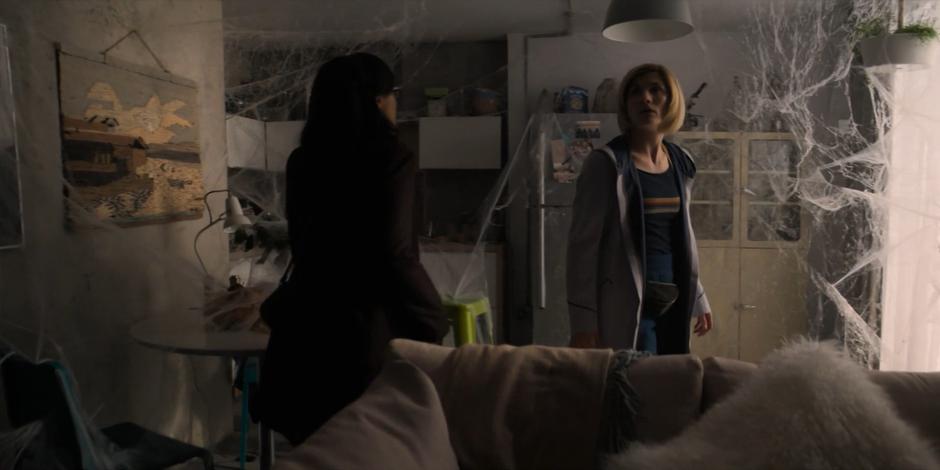 Jade and the Doctor look around the web-covered interior of the apartment.