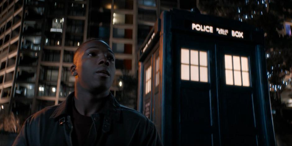 Ryan stands by outside the TARDIS in the evening.