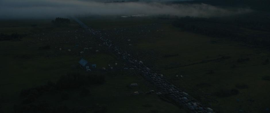 A long line of cars blcok the street leading up to a roadblock surrounded by a mass of people.