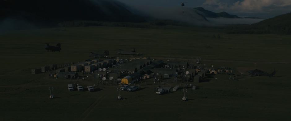 Several military helicopters arrive at the camp sitting in the middle of a farm.