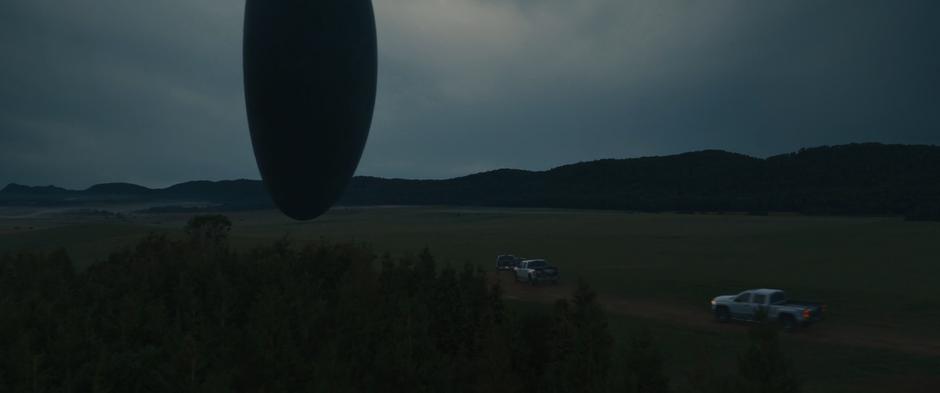 Several pickup trucks drive across the hill and over to the alien craft.