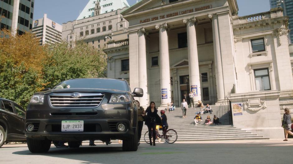 Mel pulls Maggie over to her car parked out front of the building.