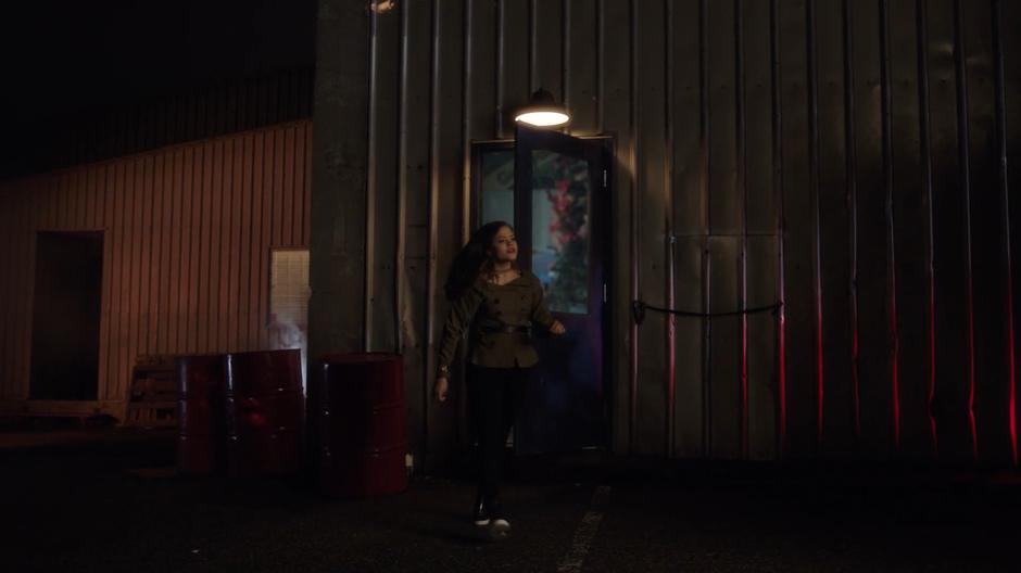 Maggie walks out of the door of the warehouse and looks around.
