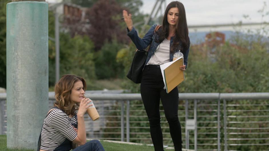 Nina stands up while exasperated with Izzy who looks off into the distance while drinking her iced coffee.