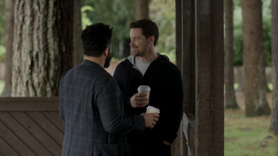 Jack turns and looks over at a woman and some children while talking with Dave in the pavilion.