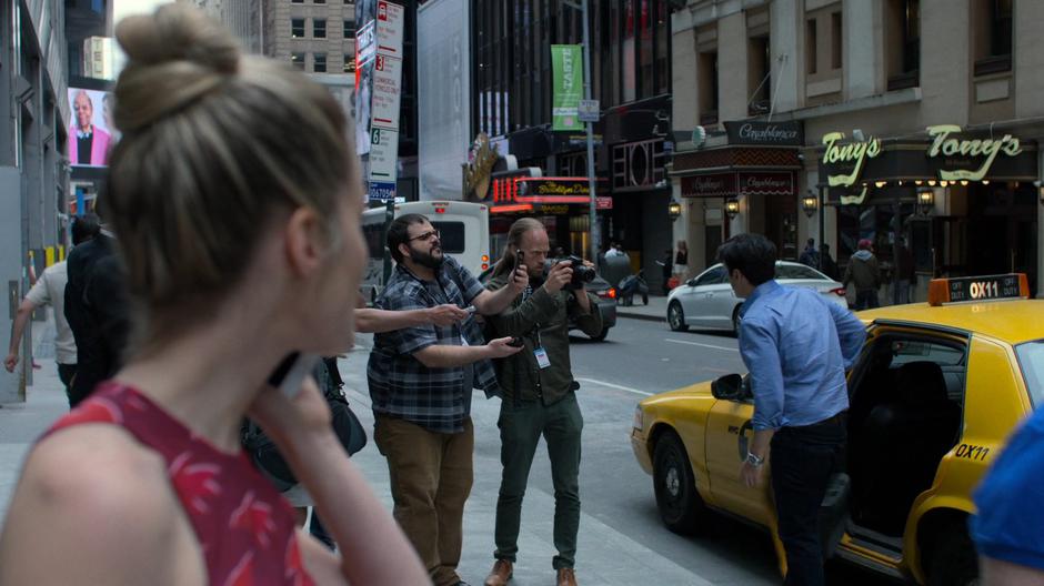 Trish looks over as Griffin is surrounded by the press while exiting his taxi.