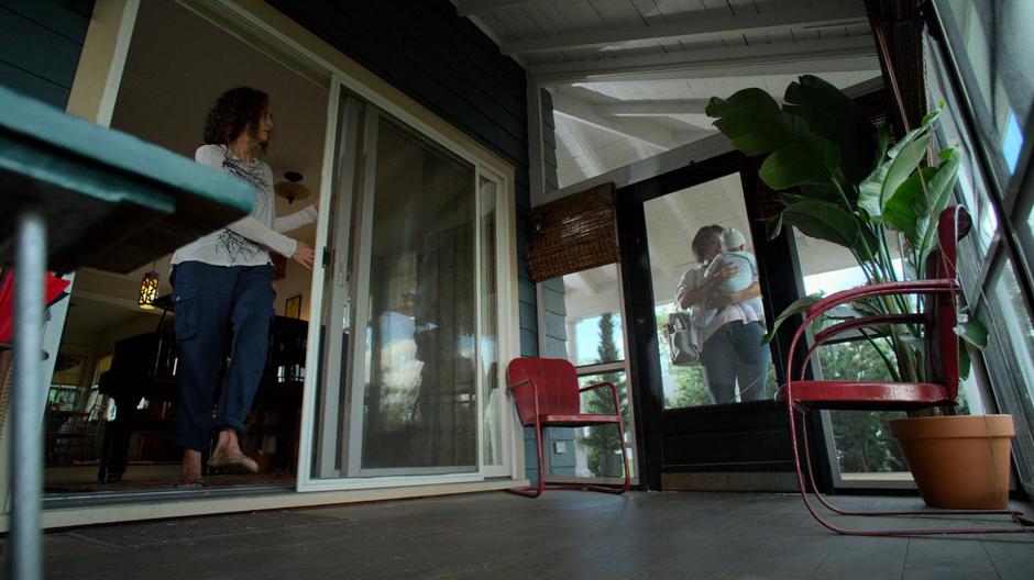 The mysterious woman opens her door as her neighbor stands outside holding her baby.