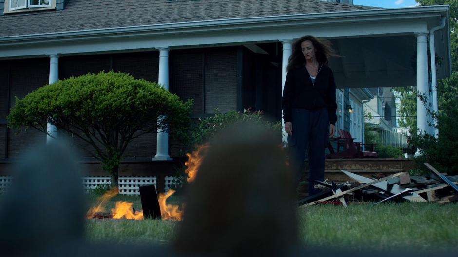 The mysterious woman stands over the burning remains of the piano she smashed to pieces.