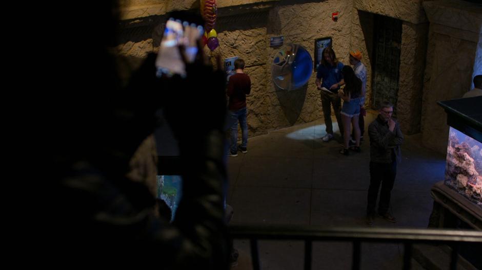 Jessica holds up her phone to take a photo of Dr. Malus from the second floor.