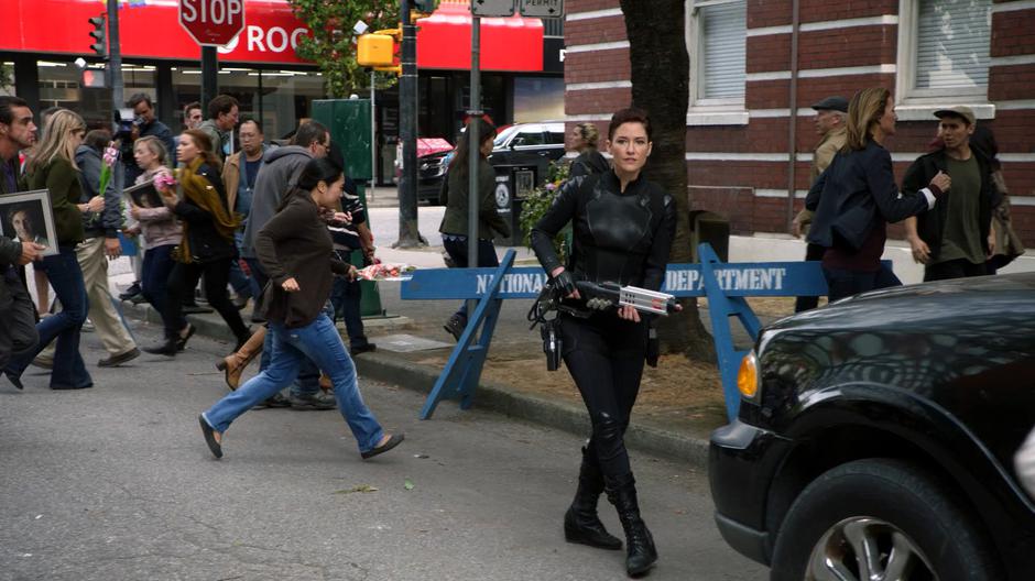 Alex strides down the street with the backpack weapon as people run around in a panic.