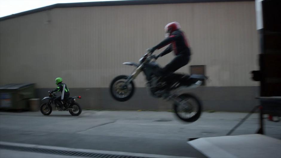 A second motorcyclist jumps out of the back of the truck and drives alongside the first.