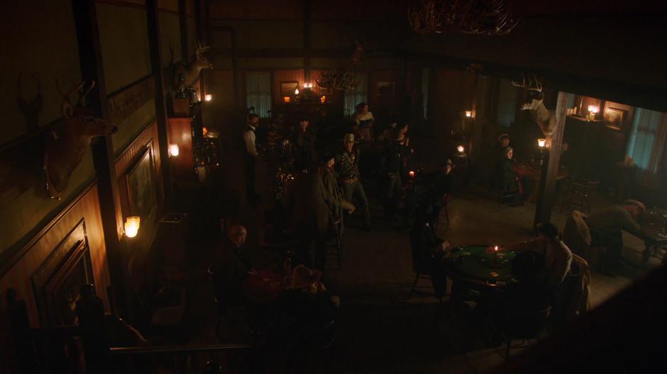 Jonah Hex wlkas around Sara and the others in the middle of the busy saloon.
