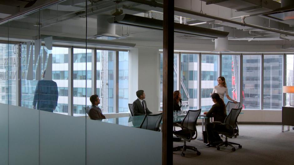 Bull looks out the window while Benny listens to J.P. Nunnelly with the rest of her team at the conference room table.