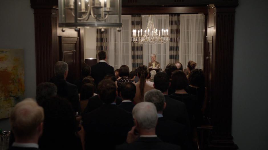 Mary does a reading on front of the crowd in the living room.