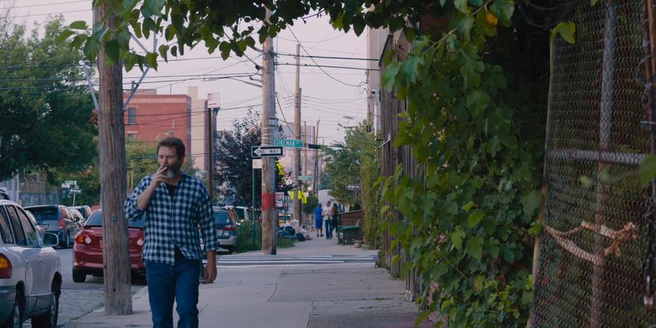 Frank smokes a cigarette while walking down the sidewalk.