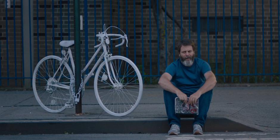 Frank sits down on the curb next to the ghost bike with the notebook he found in the apartment.