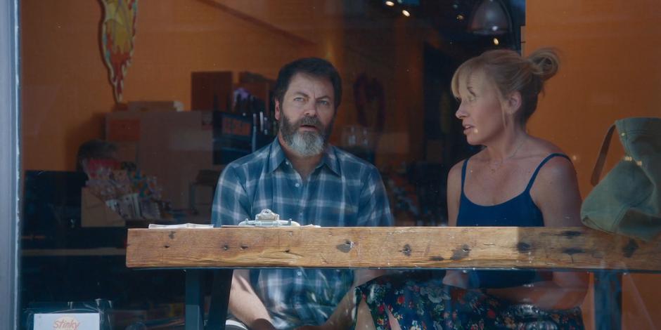 Frank talks to Leslie while they sit in the window seat of the store.