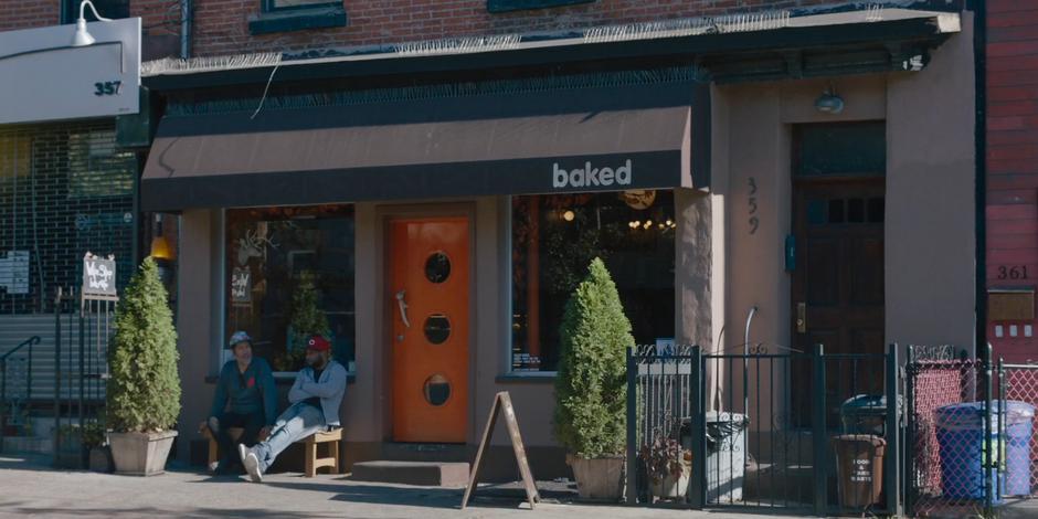 Two people sit on the bench in front of the bakery.