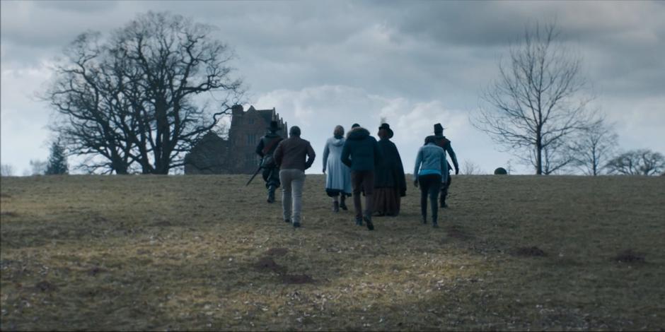 The Doctor, Becka Savage, and friends walk up the hill towards the mansion.