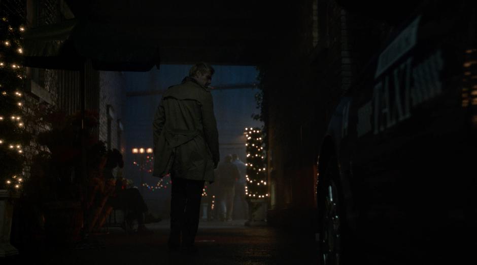 Constantine smokes a cigarette while walking down the dark alley.