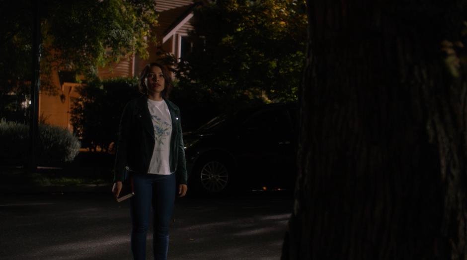 Nora stands behind a tree and looks up at her grandparents on their porch.