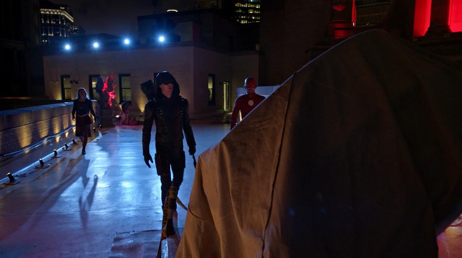 Kara, Barry, and Oliver walk over to the covered Bat-Signal.