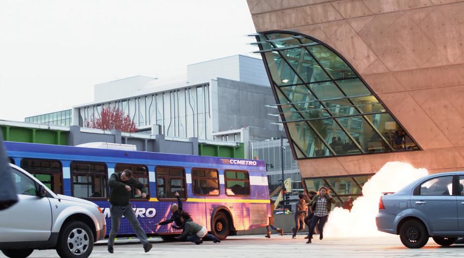 People are thrown back by an explosion against a stopped bus.