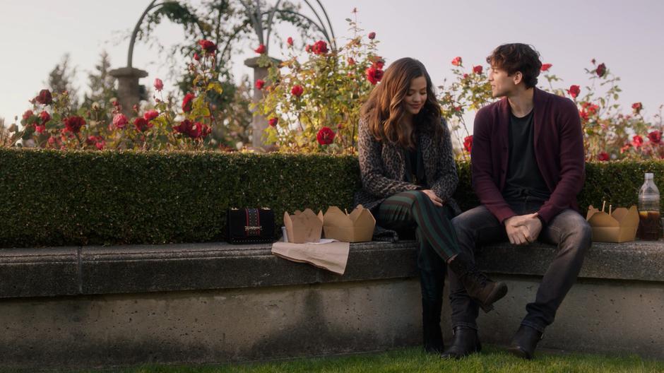 Maggie smiles down while talking to Parker on the bench after finishing their meal.