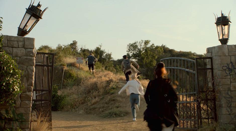 Chase, Karolina, and Nico run after Mike on a Bike up the hill past the abandoned gate.