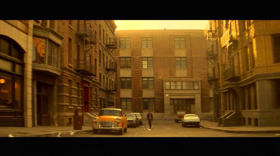 Victor walks down a deserted street past old cars.