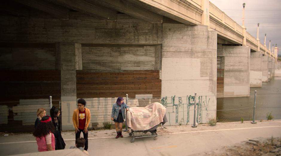 Alex checks his pockets and realizes the money is missing while standing with the other kids under the bridge.