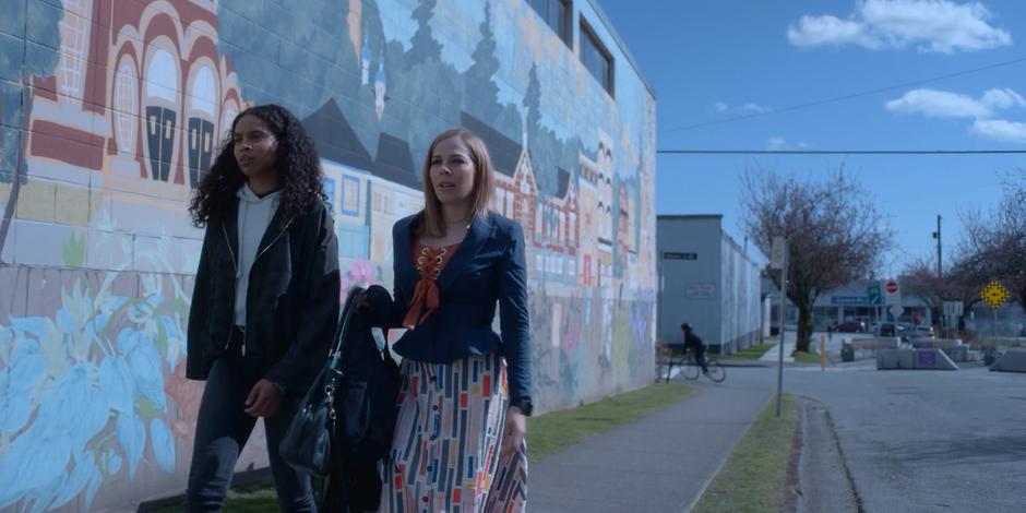 Carly and Marcy walk off with the package while the other traveler rides around the corner on his bike.