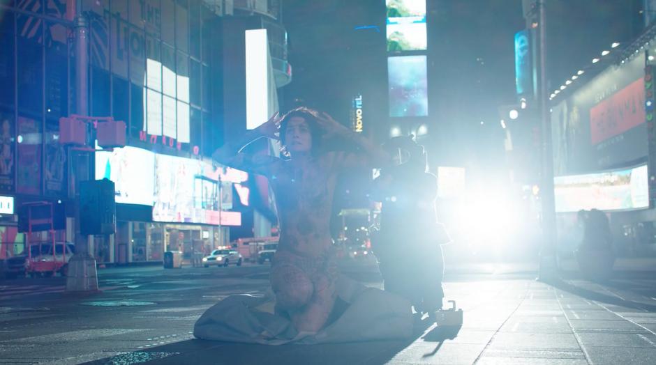 The member of the bomb squad holds the woman at gunpoint as she kneels down naked with her hands on her head.