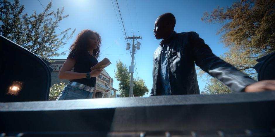 Carly hands an envelope of money over to Jeff as he loads gear into the trunk of his car.