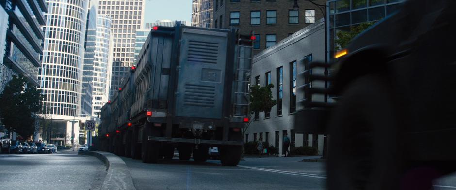 The convoy truck drives down the street surrounded by Humvees.