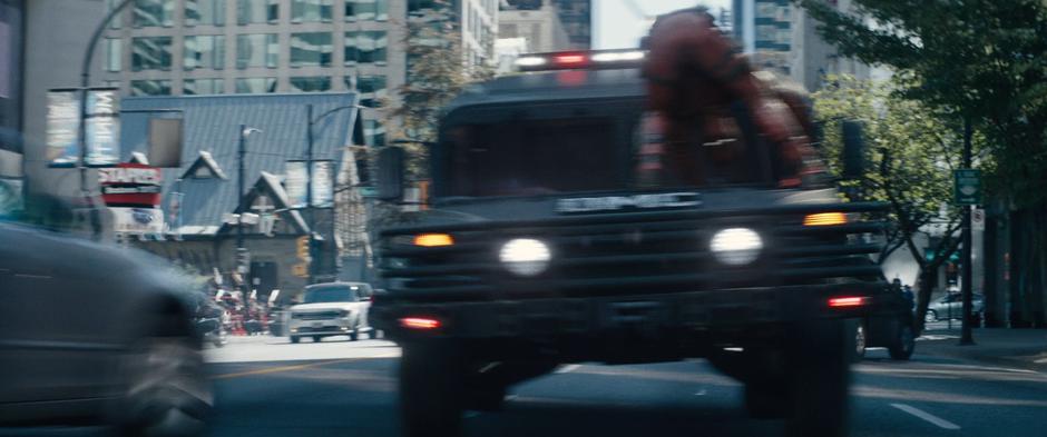 Wade looks through his legs while riding on the hood of a humvee.