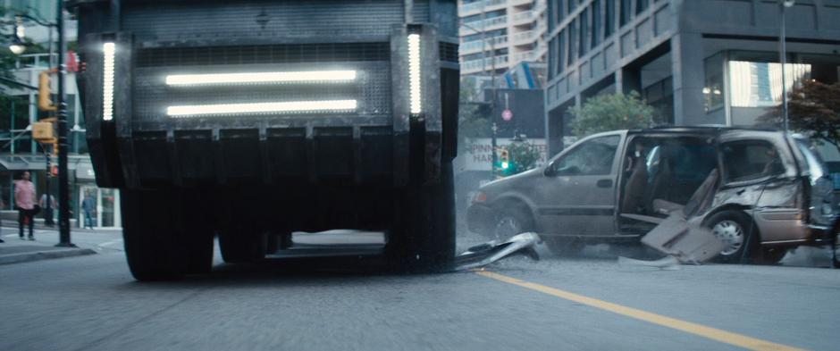 The convoy truck smashes aside a car as it drives down the street.