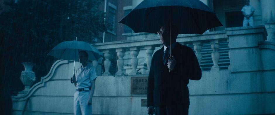 The headmaster stands in front of the facility stairs with an umbrella.