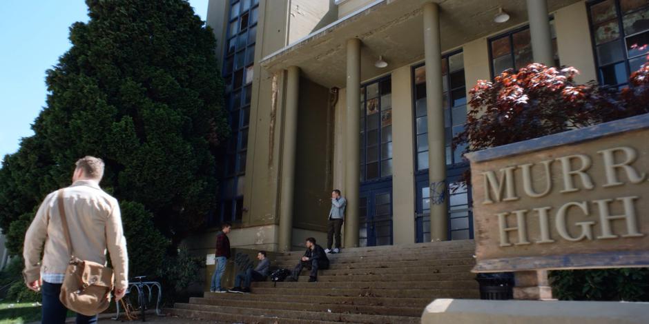 David walks down the street towards the gang who are sitting on the steps of the abandoned school.