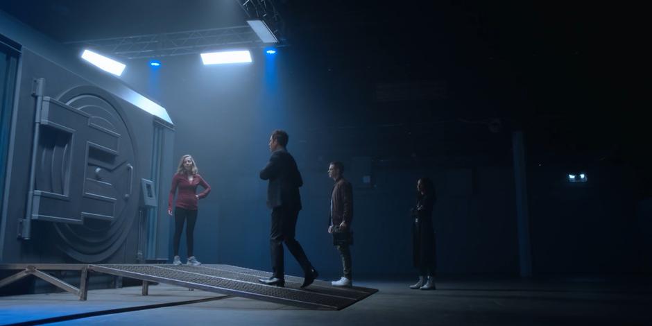 Grant, Trevor, and Carly join Marcy in front of the Archive's vault door.