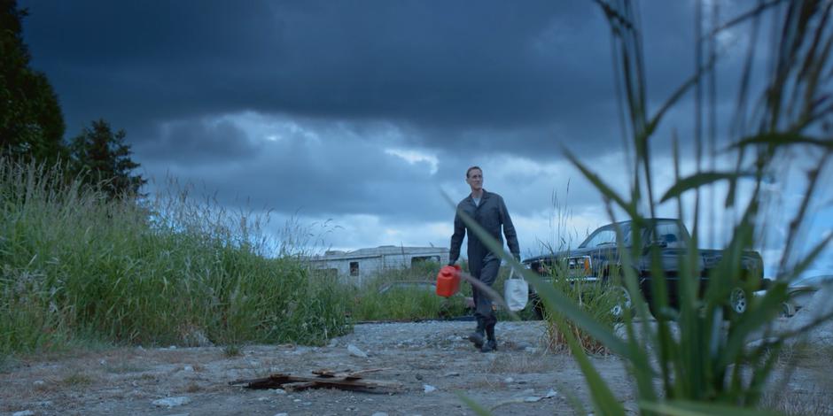 Andrew Graham walks over to a prepared pile of wood with a tank of gasoline and a bag of items.