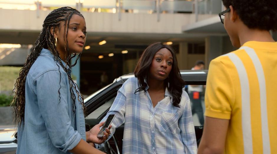 Livvie and Tamar shoot Alex a look while they stand beside the car.