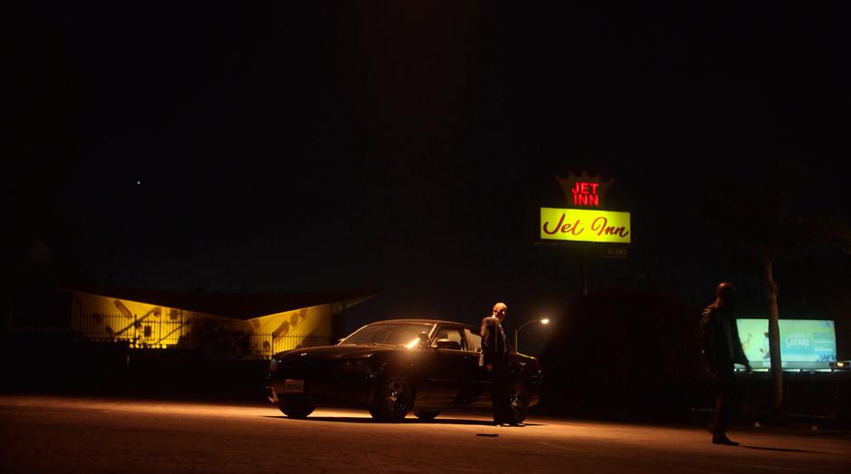 Detective Flores leans against his car as Geoffrey walks away after tossing Flores's gun on the ground.