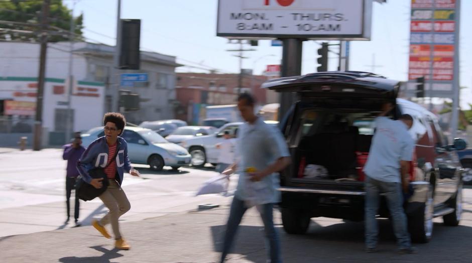 Alex turns the corner and runs through the car wash.