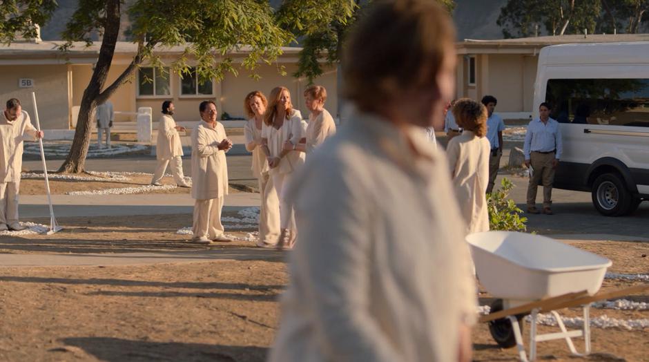 Frances and Aura pull a handcuffed Leslie through the crowd of disciples.